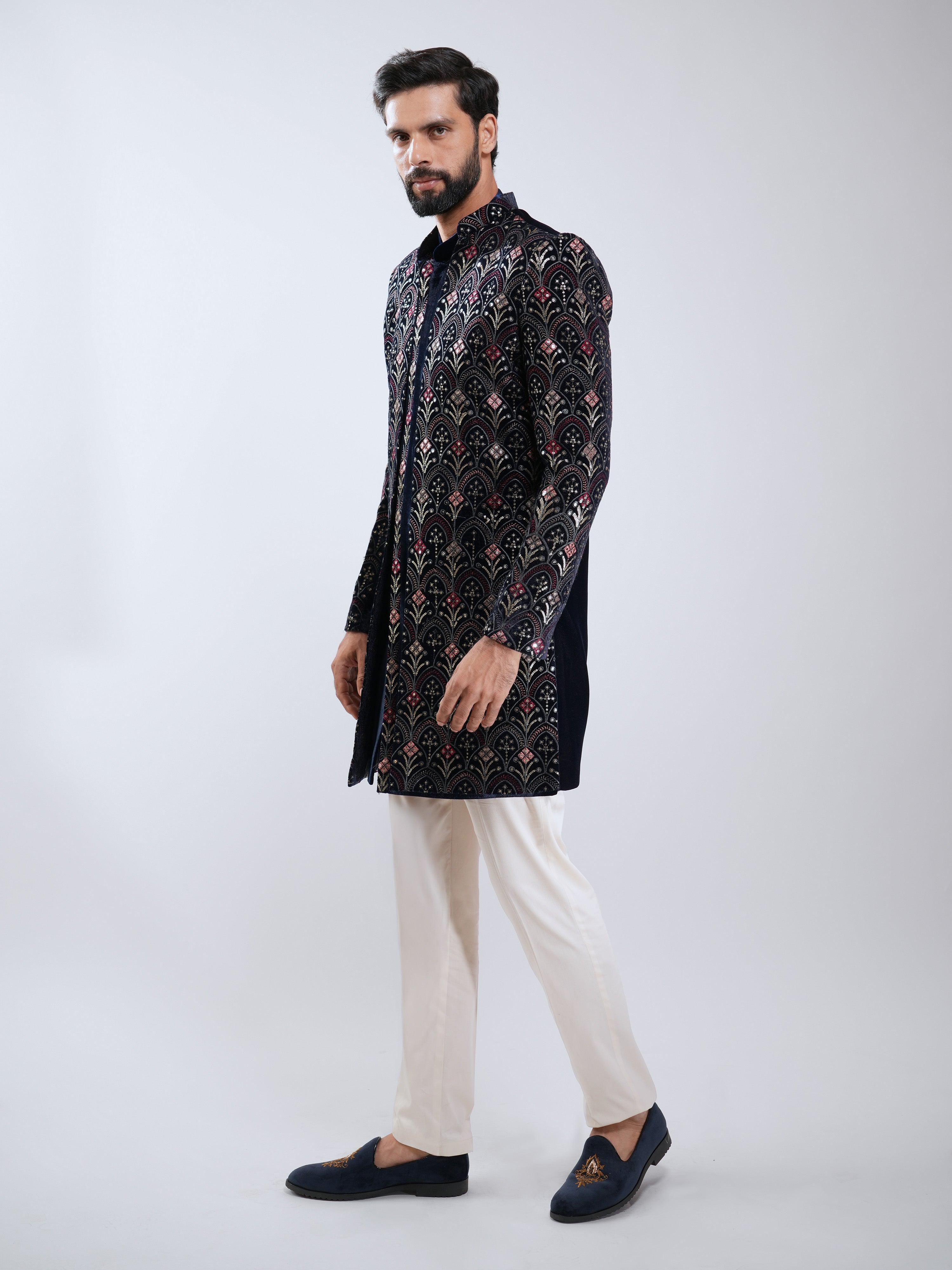 Man wearing a black patterned kurta with white pants on a light gray background