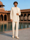Man in a cream traditional outfit standing in front of architectural ruins with water feature.