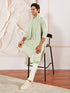 A man sitting on a stool wearing a pista green rayon kurta pyjama and dupatta set with embroidery details.