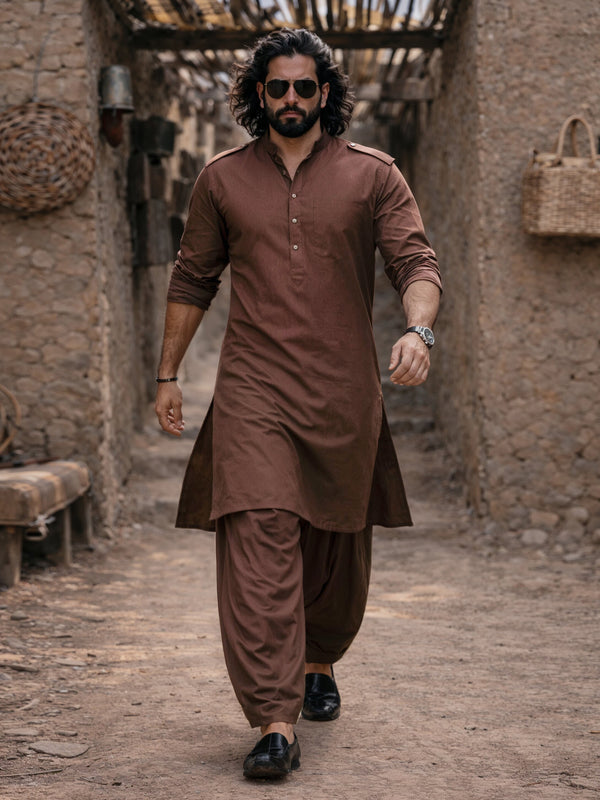 Man in a brown traditional outfit walking through a rustic alleyway.