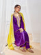 A woman sitting, wearing a traditional purple kurta set with yellow dupatta and gold embellishments.