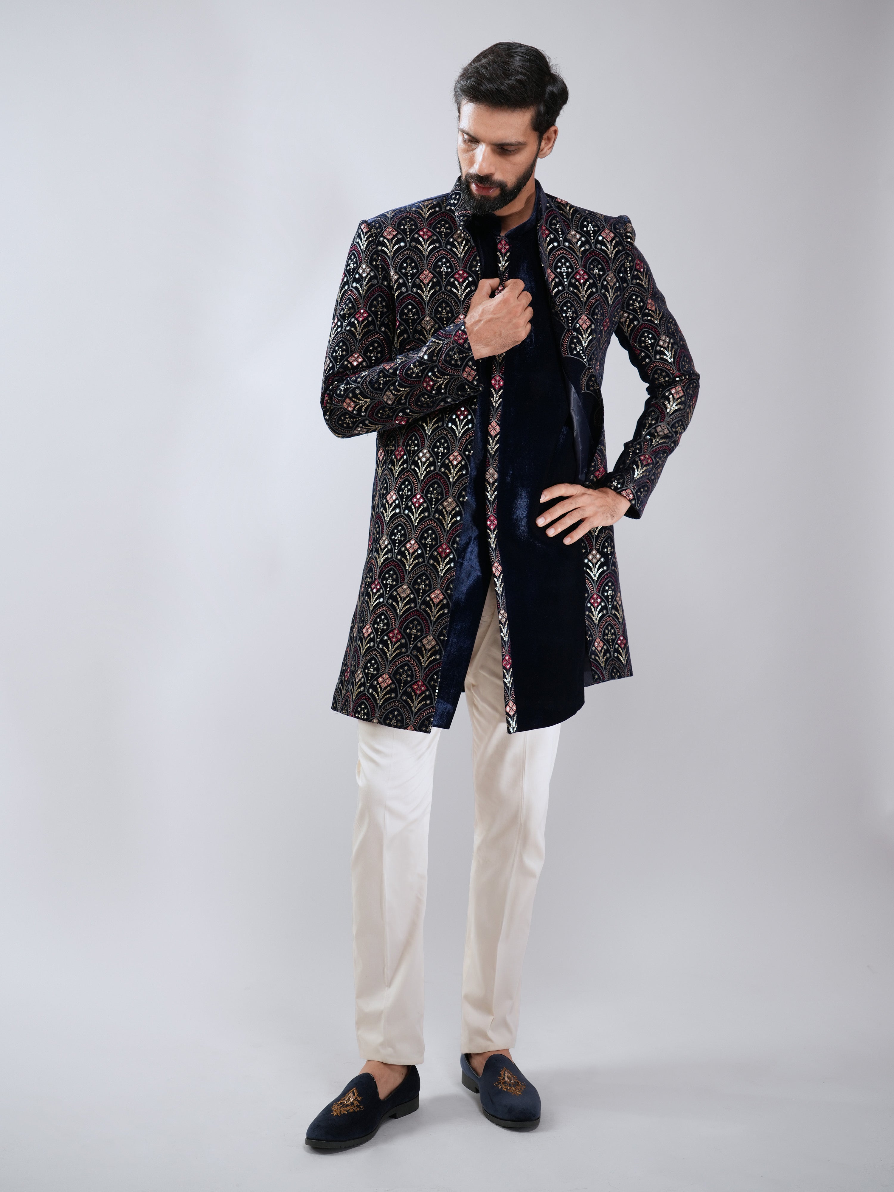 Man wearing a patterned black and gold sherwani with white pants on a gray background