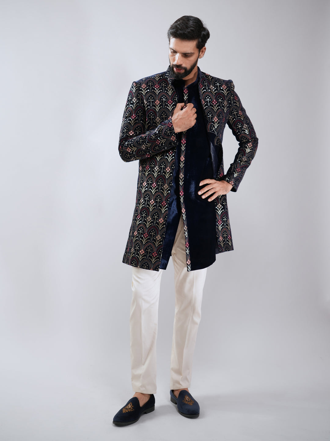 Man wearing a patterned black and gold sherwani with white pants on a gray background