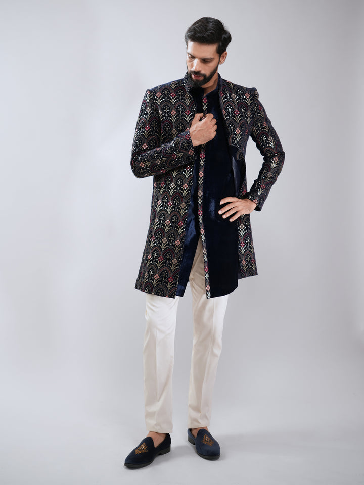 Man wearing a patterned black and gold sherwani with white pants on a gray background