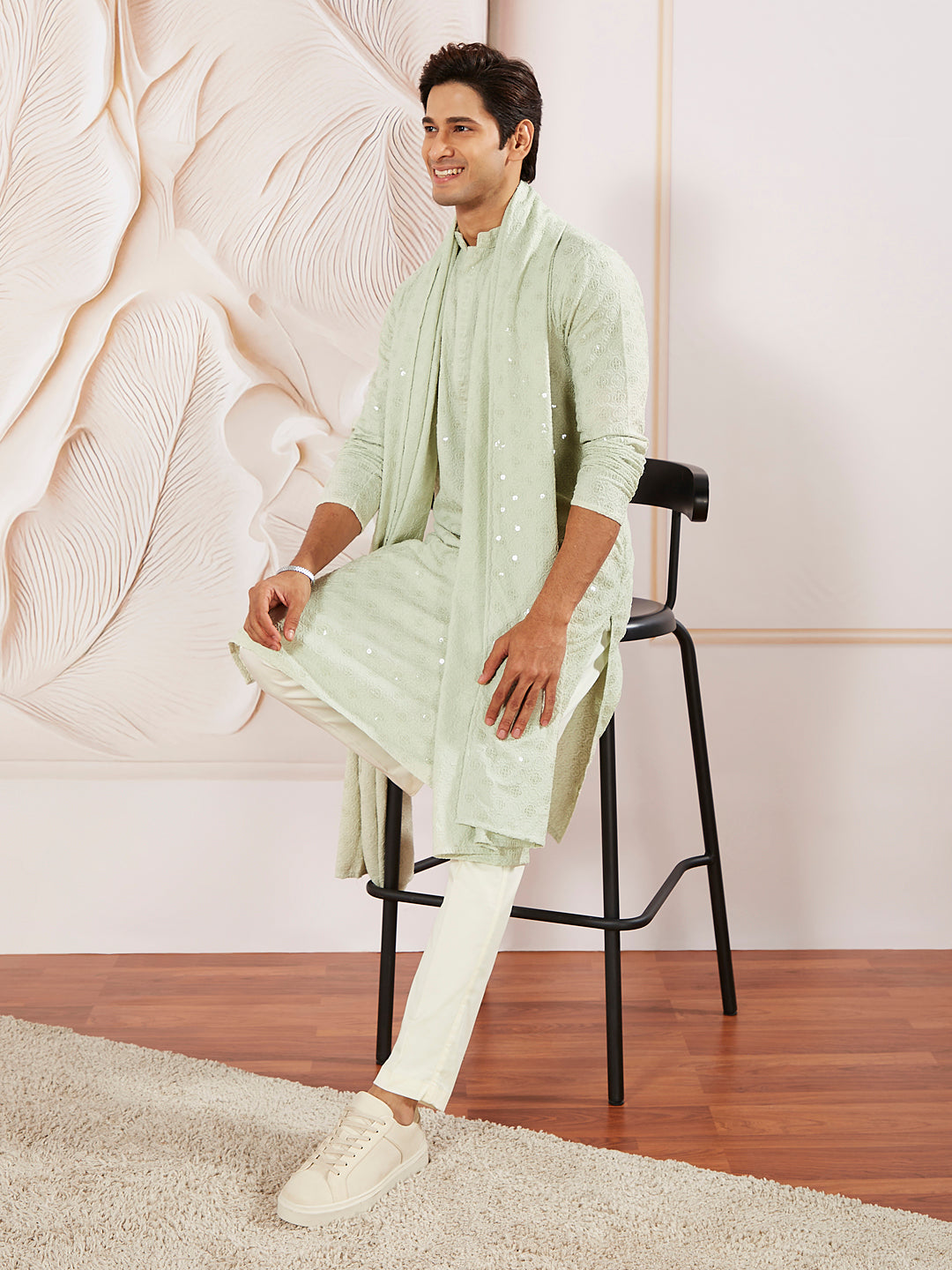 A man sitting on a stool wearing a pista green rayon kurta pyjama and dupatta set with embroidery details.