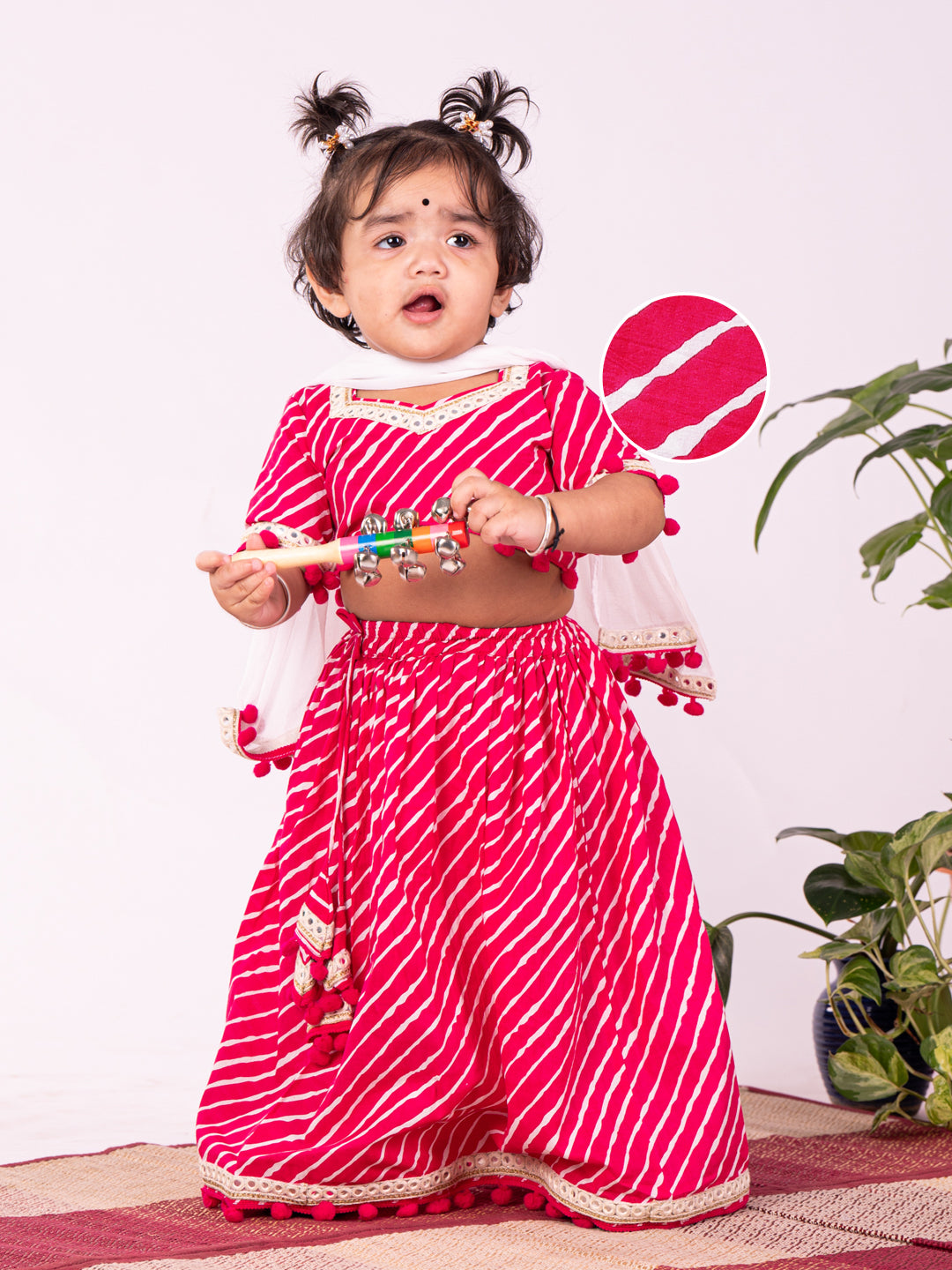 A young girl wearing a traditional pink lehenga choli with dupatta, featuring a sweetheart neck and pom pom lace detailings.